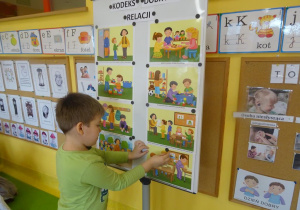 Chłopiec zawiesza na tablicy ilustracje prezentującą jedną z zasad Kodeksu dobrych relacji.